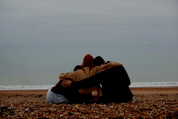 Three people hugging on a quiet beach, sharing a moment of friendship by the sea